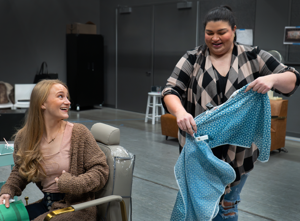 two characters sitting in a beauty shop, one in a chair and one folding up a haircut cape