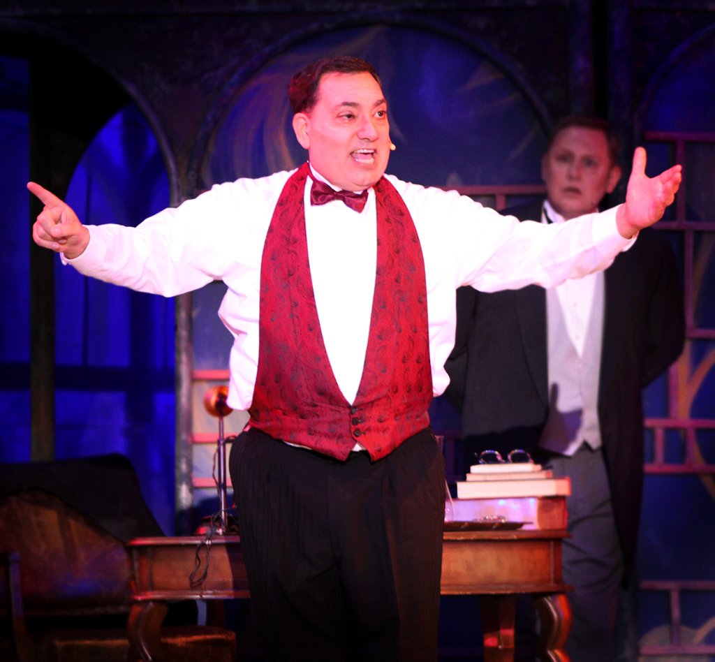 Henry higgins sitting in study singing with his arms up