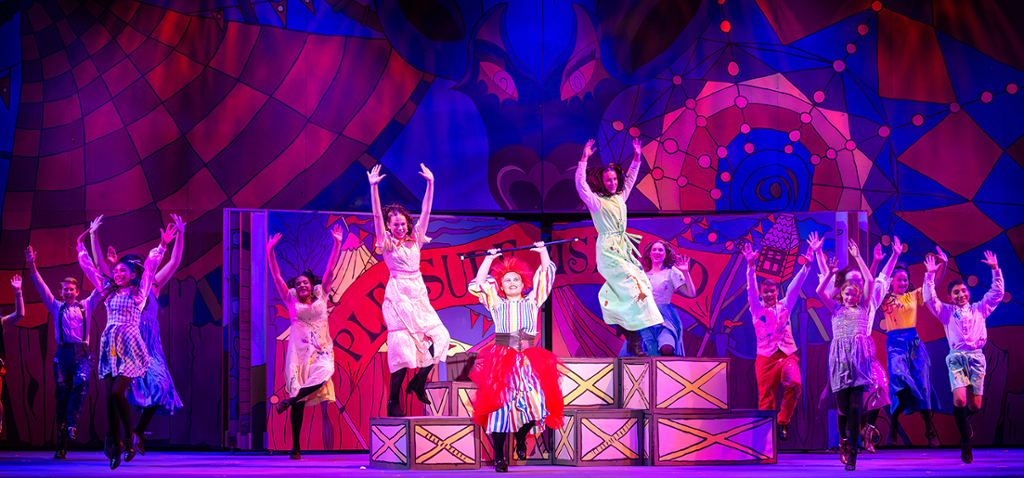 large group of actors in pinocchio dancing in front of a giant scary circus