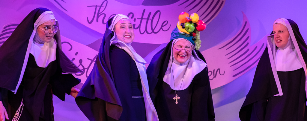a line of nuns dancing and one has a bowl of fruit on her head.
